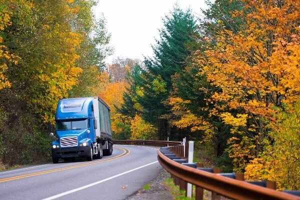 Semi truck driving down a road while the leaves change colors
